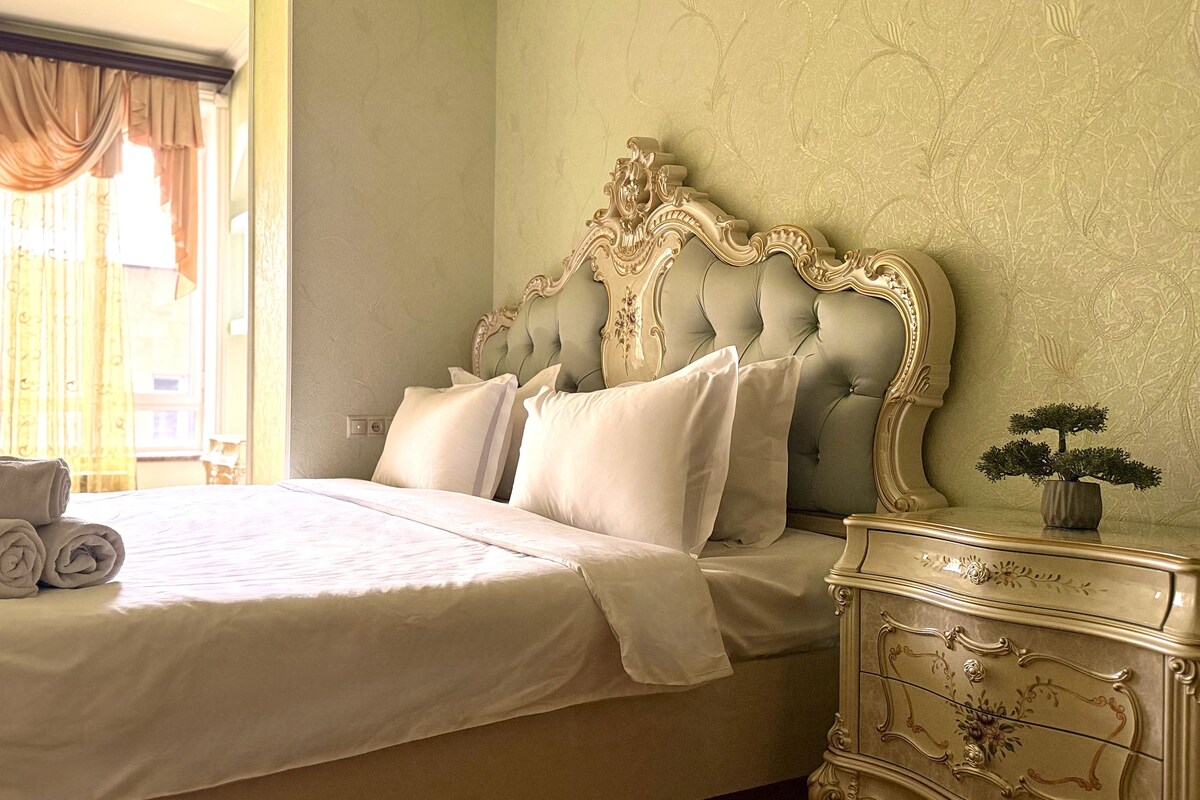 A neatly made bed with pillows and a rolled towel, a dresser with drawers, and a small potted plant on the dresser.