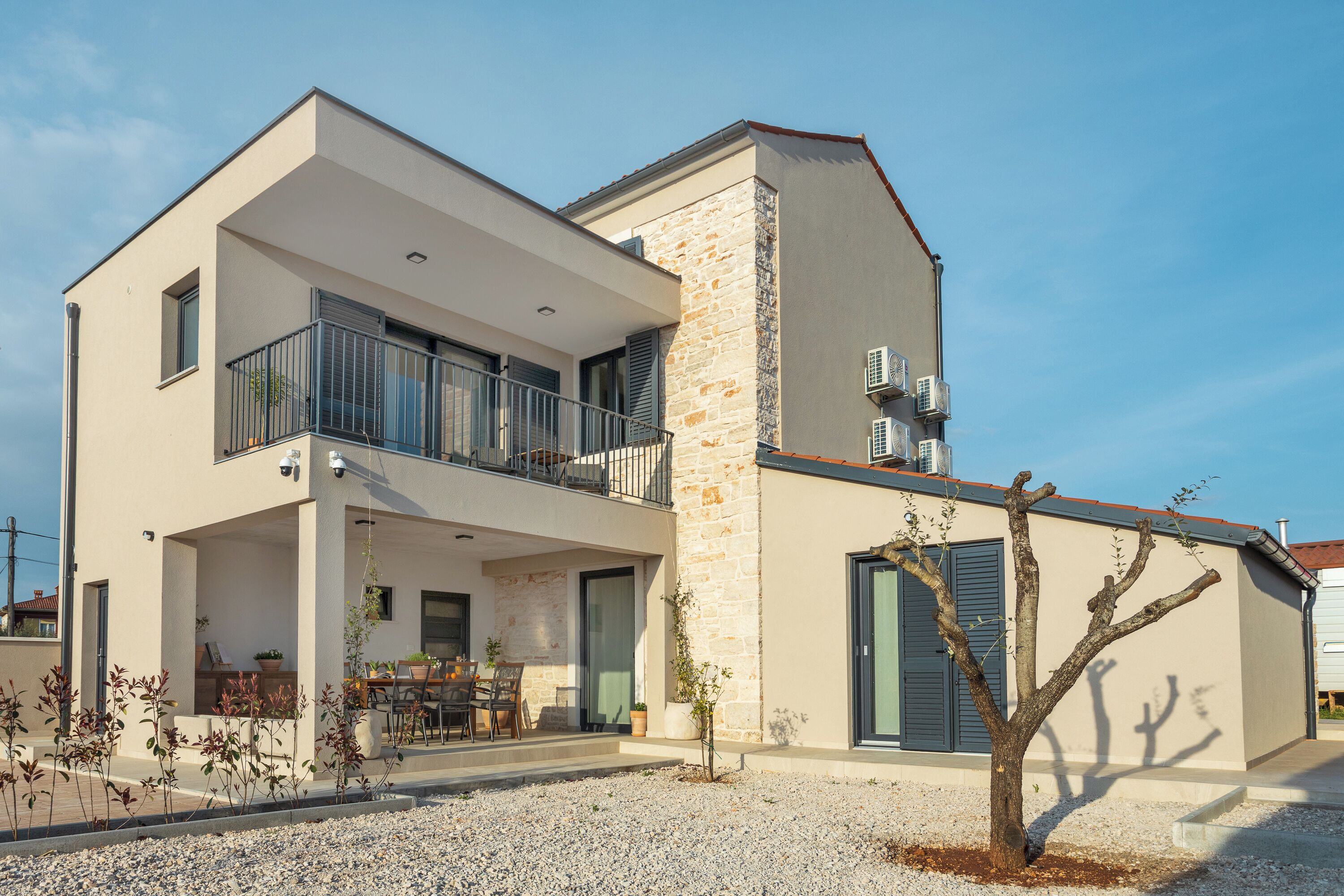 Un bâtiment moderne à deux étages, doté d’un balcon, d’une façade en pierre et d’une allée gravillonnée.