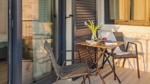 Un patio con una mesa, dos sillas, un florero con flores y una ventana con persianas.