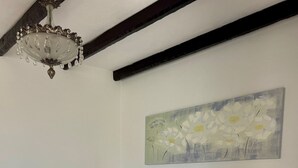 Un dormitorio con una cama blanca, ropa de cama floral, un cuadro de flores, una araña y una viga de techo de madera.