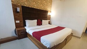 A neatly made bed with a wooden frame, a red quilt, and white linens. There is a nightstand with drawers and a lamp on the wall. - Collection O Lansdowne Viewpoint (Lansdowne)