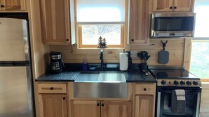 A compact kitchen with wooden cabinets, a stainless steel refrigerator, a microwave, a stove, and a window with a view.