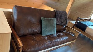 A brown leather sofa with two cushions, a wooden bench, and a small table in a cabin with wooden walls and a sloped ceiling.