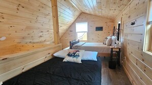 A cabin with two beds, wooden walls, a sloped ceiling, and a window.