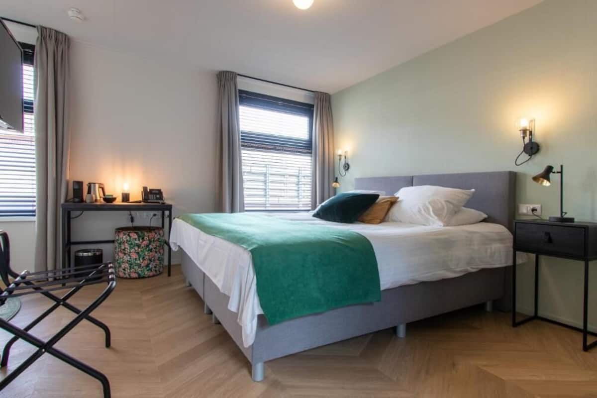 Ein Schlafzimmer mit Bett, Nachttischen, einem Sessel, einem Fenster mit Vorhängen und einer Lampe.