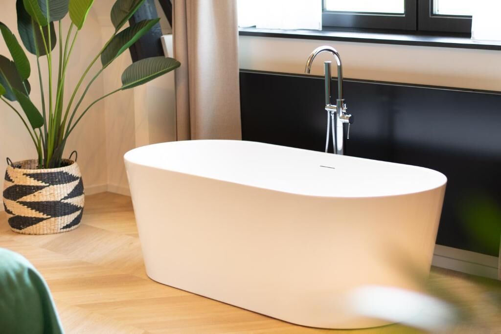 Un baño moderno con una bañera independiente, una planta en maceta y un ventanal con cortinas.