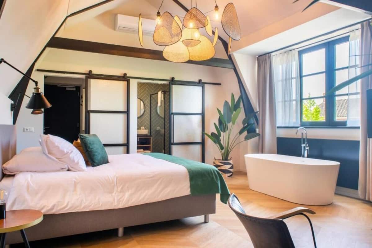 Ein modernes Schlafzimmer mit Bett, großem Fenster, Badewanne und einer Pflanze.