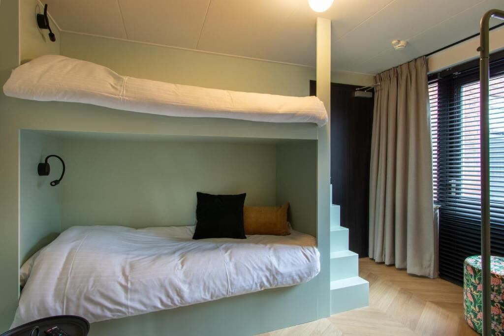 A bunk bed with a white mattress, a black pillow, and a beige pillow. There is a small table with a floral tablecloth.