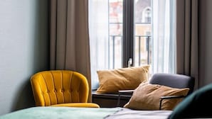 Een kamer met een gele fauteuil, een blauwe fauteuil en een raam met gordijnen.