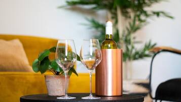 A table with two wine glasses and a copper decanter, a potted plant, and a yellow sofa in the background.