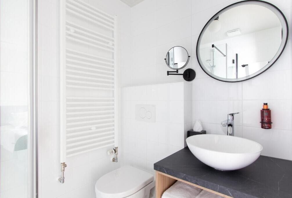 A modern bathroom with a white toilet, a round mirror, a white sink, and a towel rack.