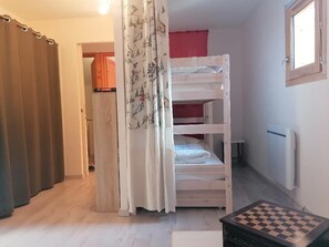 Ein Zimmer mit Etagenbett, Heizkörper, Fenster, einer Vorhang-ausgestatteten Tür und einem Schachbrett.