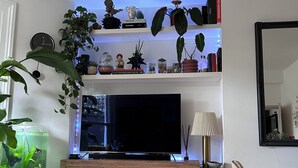 Ein Wohnzimmer mit Flachbildfernseher, Holzschrank, Bücherregal und einer großen Küstertanne.
