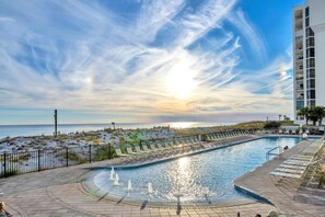 A swimming pool with a curved design, surrounded by lounge chairs and a fence. - ⛱️Pelican Beach 1611 - Seabreeze Sixteen | Gulf Views | 3 Pools⛱️ (Destin)