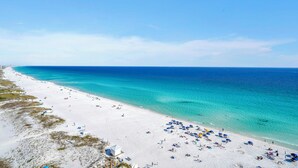 Ein Strand mit weißem Sand, klarem türkisblauem Wasser und einigen Sonnenschirmen und Liegestühlen.