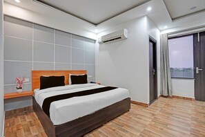 A modern hotel room with a large bed, a bedside table, an air conditioning unit, and a view through a window. - Super Townhouse Sector 9 Gurgaon (Gurugram)
