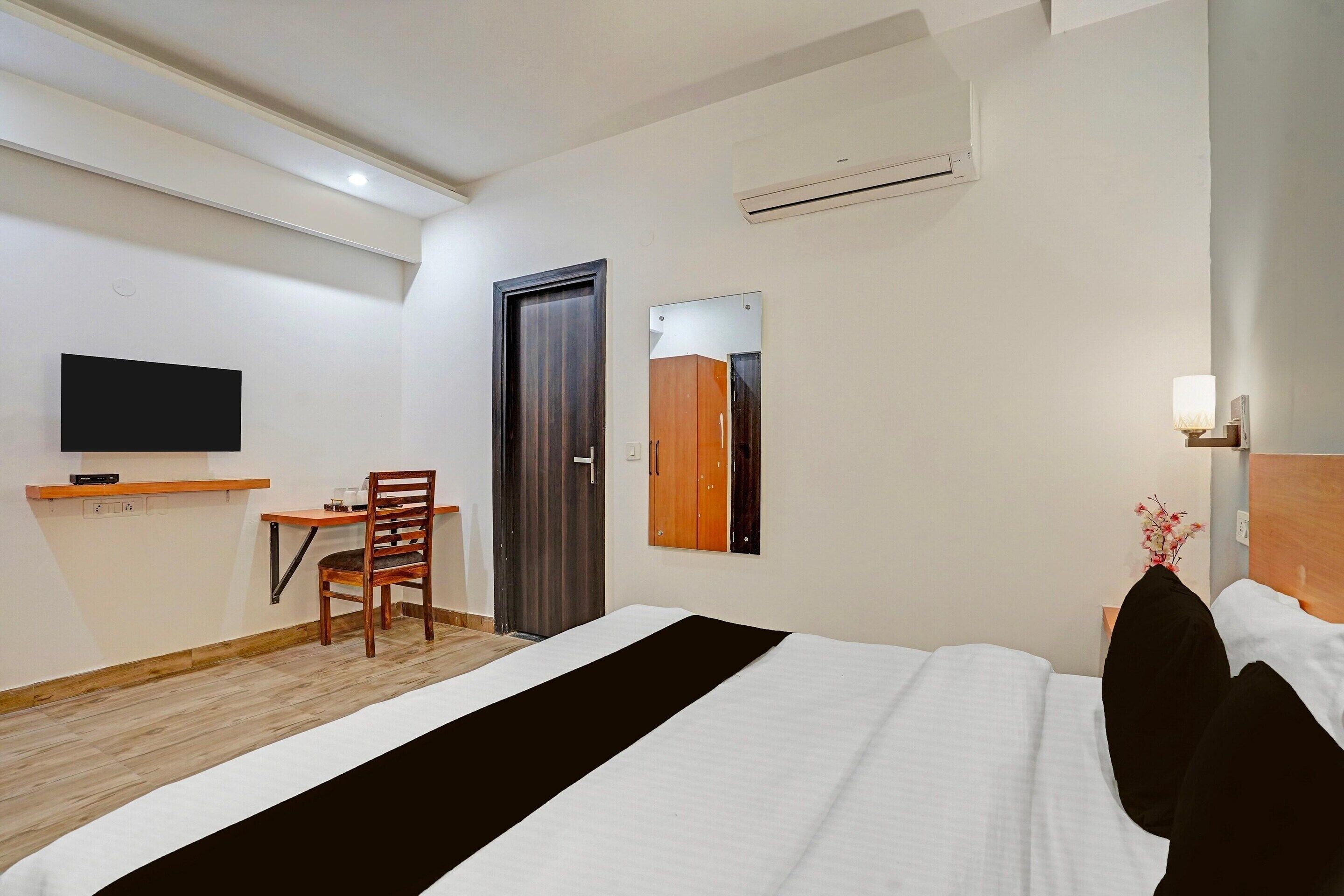 A hotel room with a bed, a desk with a chair, a television, a wardrobe, and a mirror.