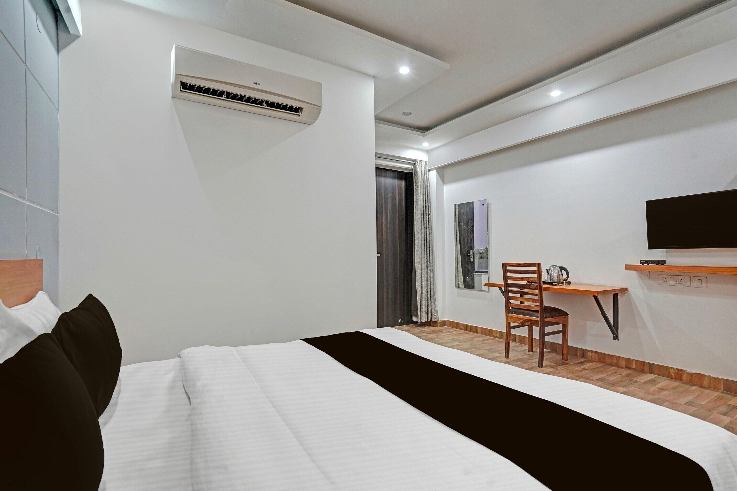 A hotel room with a bed, a desk, a chair, an air conditioning unit, and a television.