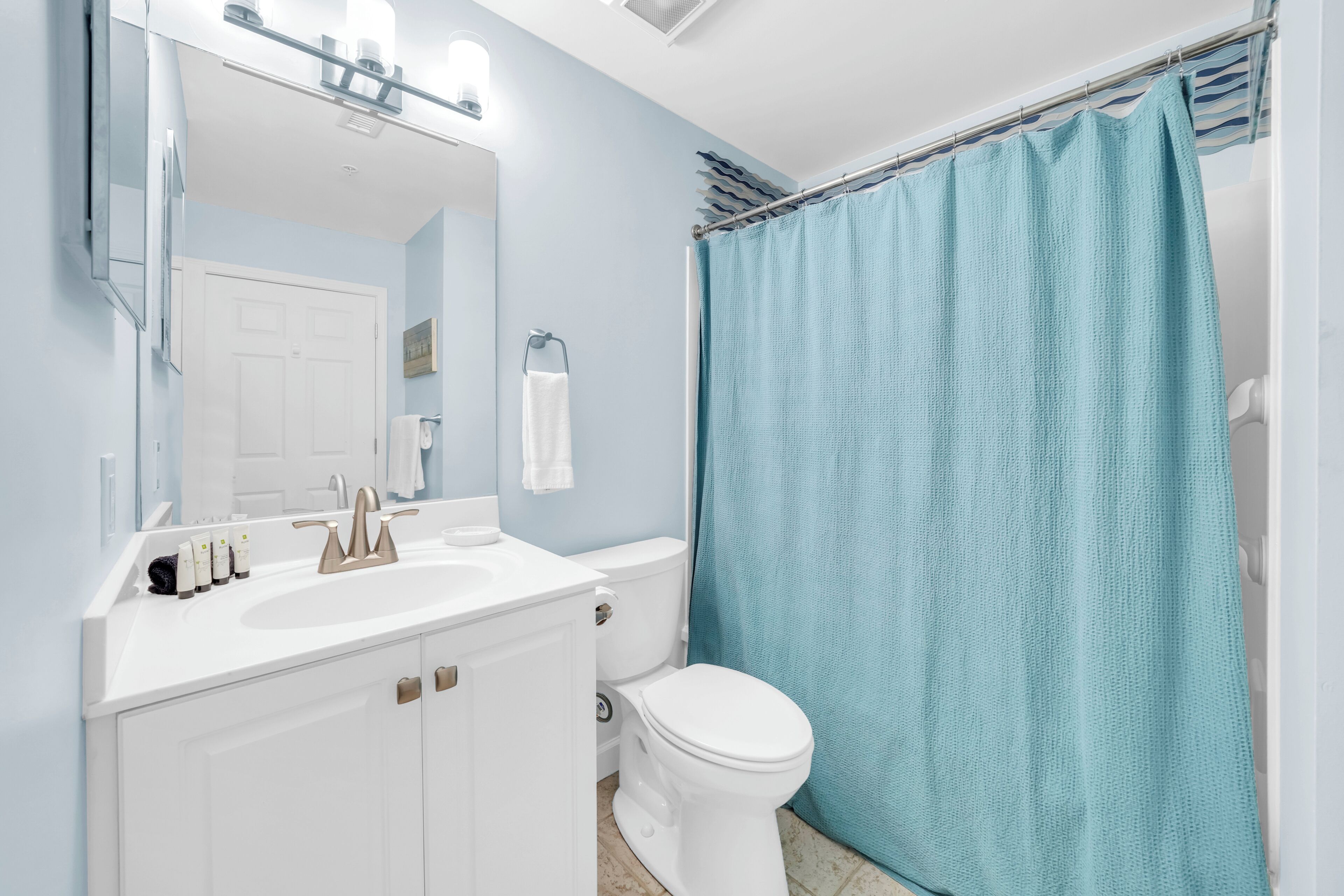 A bathroom with a white sink, a mirror, a toilet, and a blue shower curtain.
