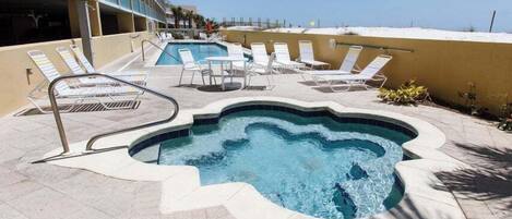 A pool area with lounge chairs and a hot tub, surrounded by a building with balconies.