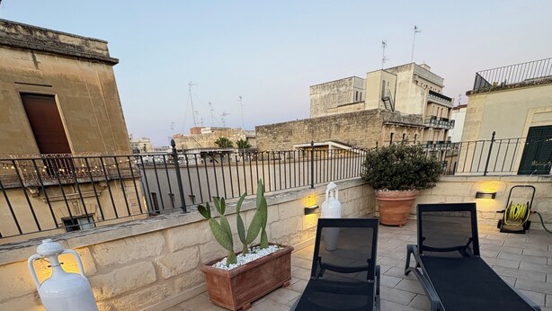 Una terraza en la azotea con dos sillones de descanso, una planta en maceta y un jarrón decorativo.