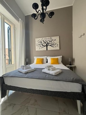 A hotel room with a bed, a chandelier, a painting of a tree, and a view of the outside. - La Fitolacca B&B (Lecce)