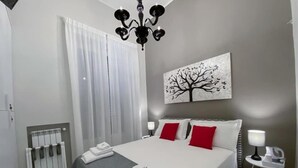 Habitación de hotel moderna con cama, radiador, una obra de arte colgada en la pared y una mesita de noche con lámpara.