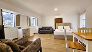 A modern hotel room with a bed, a sofa, a dining table, and a TV. - Dino's Sea View (Porto da Cruz)