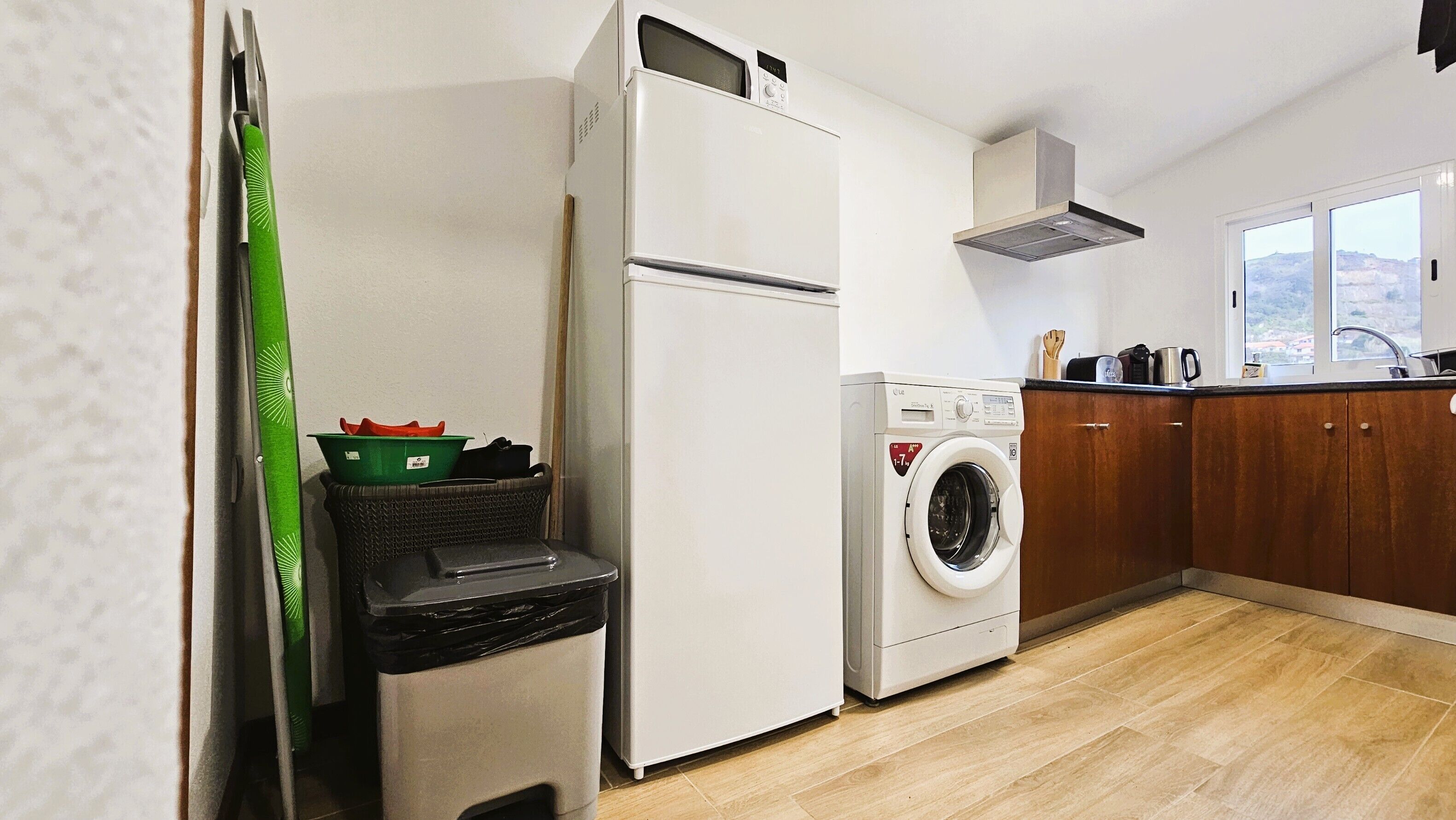 A compact kitchen with a refrigerator, washing machine, and wooden cabinets.