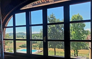 A room with large windows offering a view of a swimming pool and surrounding landscape. - Villa Piemonte - Romantik Country House in the Piedmont Vineyards (Cà Mogna)