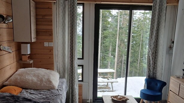 A cozy cabin with a bed, a table, a chair, and a view of a snowy outdoor area. - Praloup 1600 Studio ground floor with exterior (Uvernet-Fours)