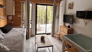 A room with a bed, a table, a TV, and a view of the outdoors. - Praloup 1600 Studio ground floor with exterior (Uvernet-Fours)