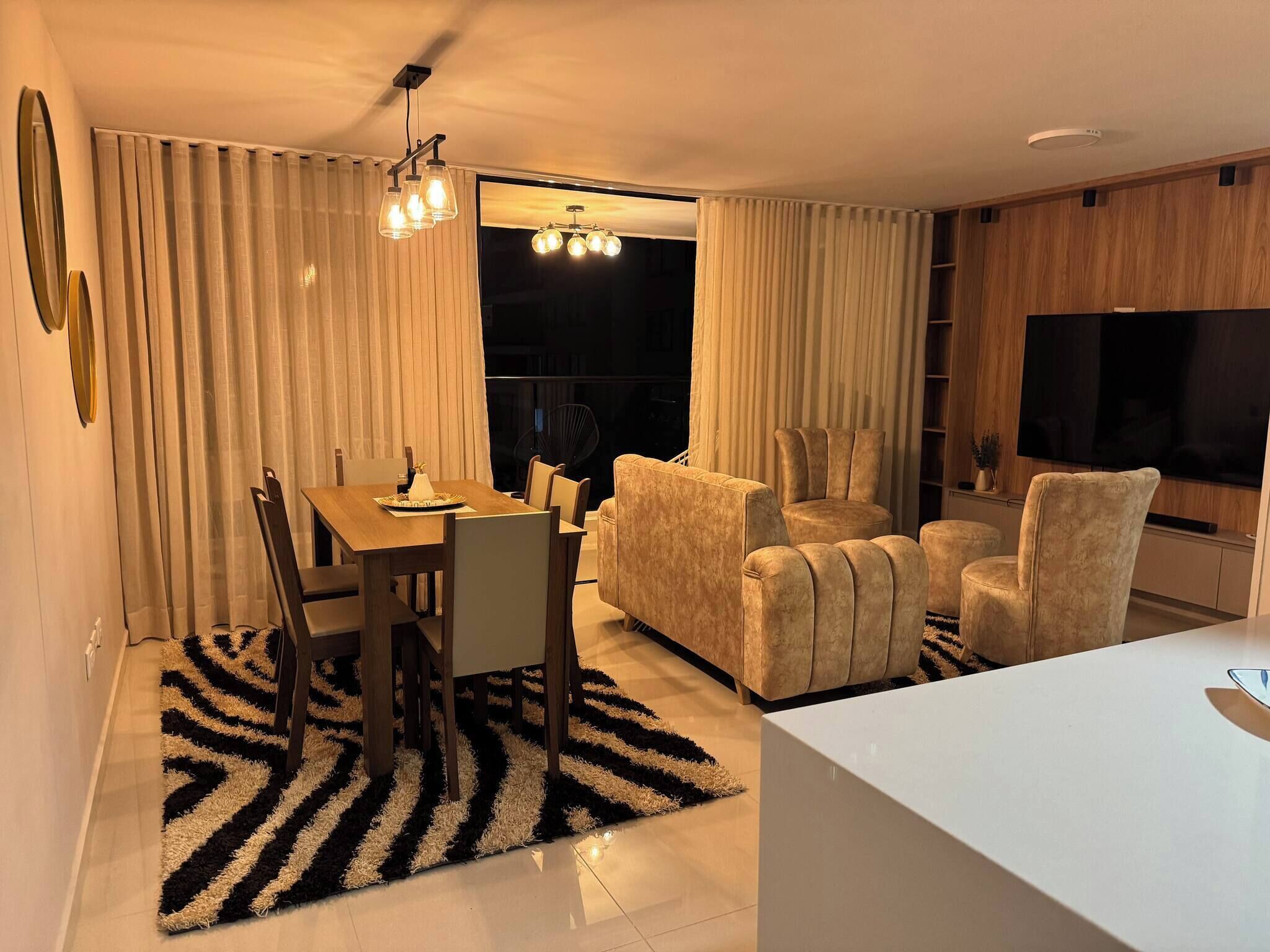 Uma sala de estar moderna com área de jantar, sofá, televisão e uma janela grande.