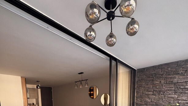 Un espace de vie moderne comprenant un canapé, une table à manger, des chaises et un luminaire au plafond au design original.