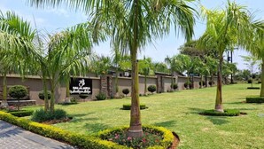 Zona ajardinada con palmeras, un sendero pavimentado y un edificio con un letrero que dice 'BALAJANTA by Fendi's Hotel'.