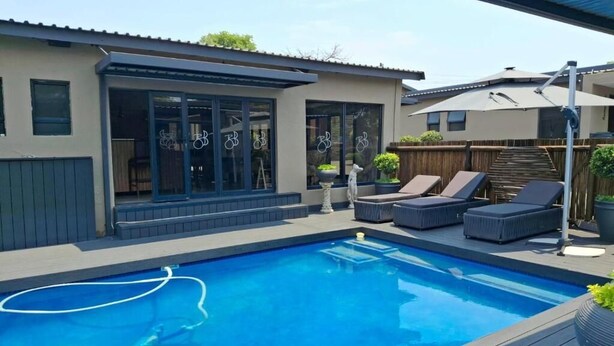 Una casa moderna con piscina, mobiliario exterior y un patio cubierto.