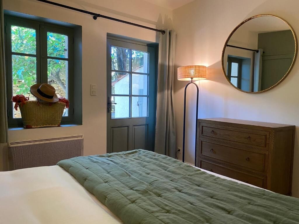 Une chambre à coucher comprenant un lit, une commode, un miroir, une lampe et une fenêtre donnant sur un paysage verdoyant.