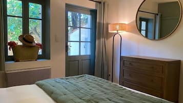 A bedroom with a bed, a dresser, a mirror, a lamp, and a window with a view of greenery.