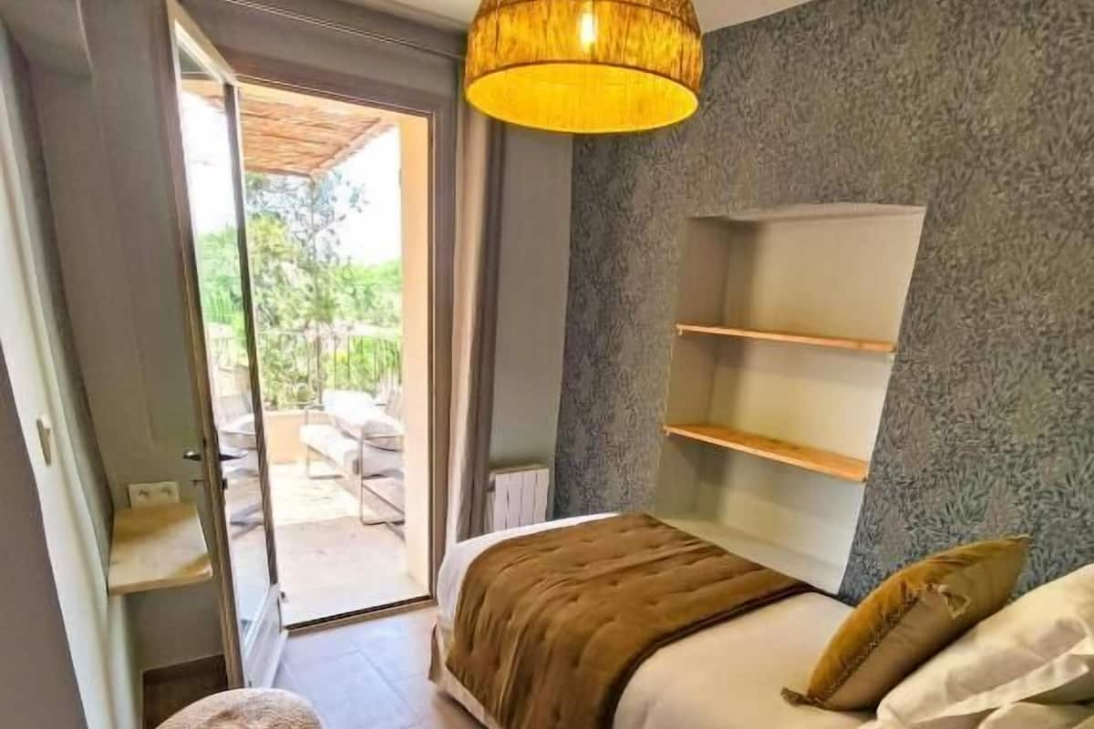 Una camera da letto con un letto, mensole a lato del letto, un lampadario a sospensione, un poggiapiedi rotondo e vista sull'esterno.