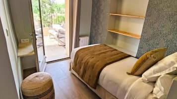 Un dormitorio con una cama, estantes junto a la cama, una lámpara colgante, un otoman redondo y vistas al exterior.