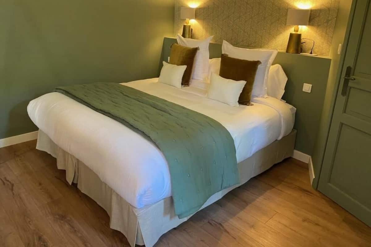 Un letto rifatto con cura, una coperta verde, due lampade da comodino e un pavimento in legno.