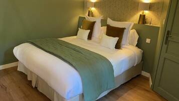 Una cama bien hecha con un plaid verde, dos lámparas de noche y piso de madera.