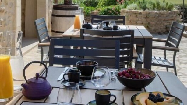 An outdoor dining area with a table set for breakfast, a stone wall, and a view of the countryside. - Domaine de Montine - Chambres de Charme (Grignan)