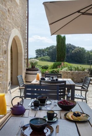 Un espacio de comedor al aire libre con una mesa dispuesta para el desayuno, un muro de piedra y vistas al campo.