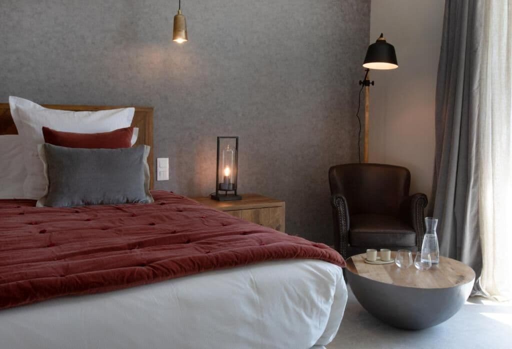 A hotel room with a bed, bedside table, lamp, chair, and a round coffee table.