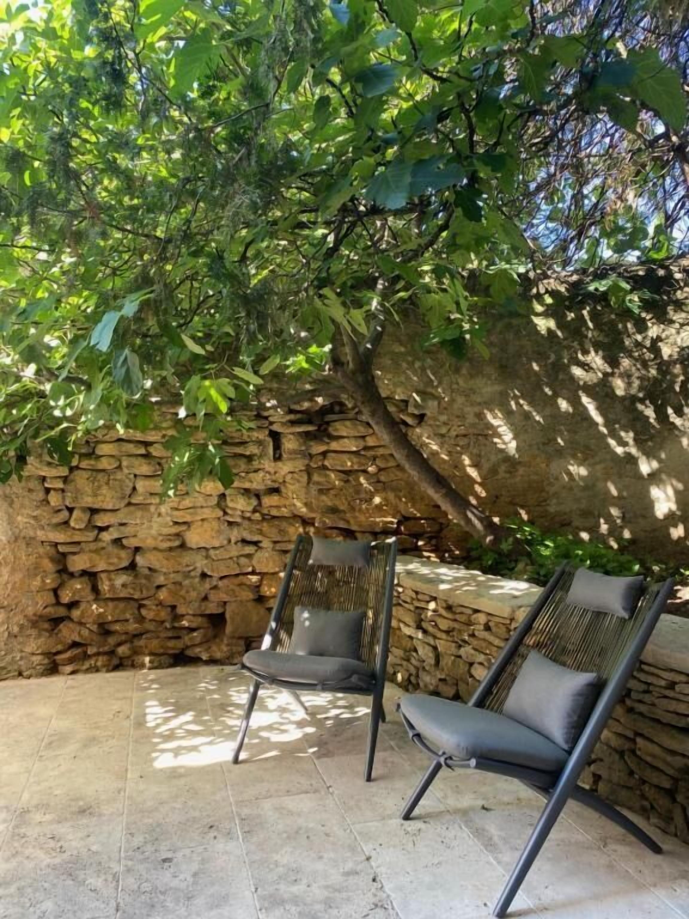 A stone wall, two lounge chairs, and a tree providing shade.
