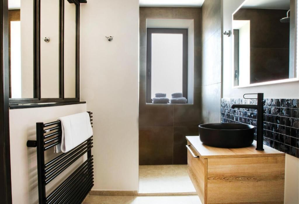 Un baño moderno con un toallero negro, un tocador de madera, un espejo grande y una ventana con toallas.