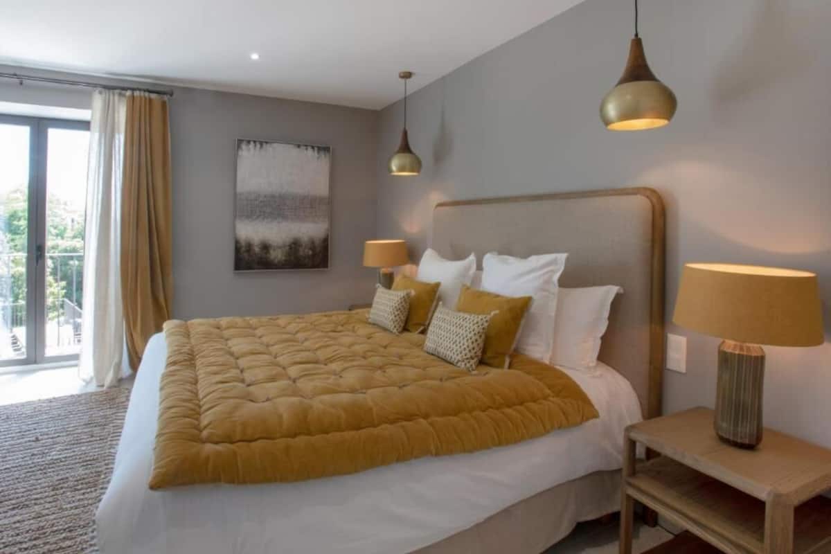Un letto grande con copriletto giallo, due lampade ai comodini, un quadro appeso al muro e vista dalla finestra.