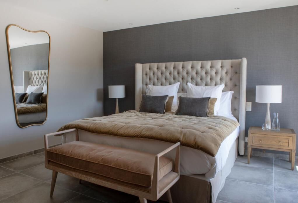 A bedroom with a large bed, two bedside tables, a mirror, and a bench.