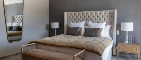A bedroom with a large bed, two bedside tables, a mirror, and a bench.